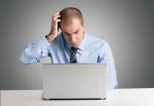 confused man scratching his head while working on a computer